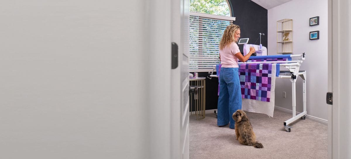 A quilter at the Super Sixteen in a spare bedroom while her dog watches from the doorway